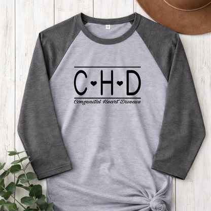 Gray and black baseball shirt with 'C-H-D' and 'Congenital Heart Disease' text on a wooden surface.